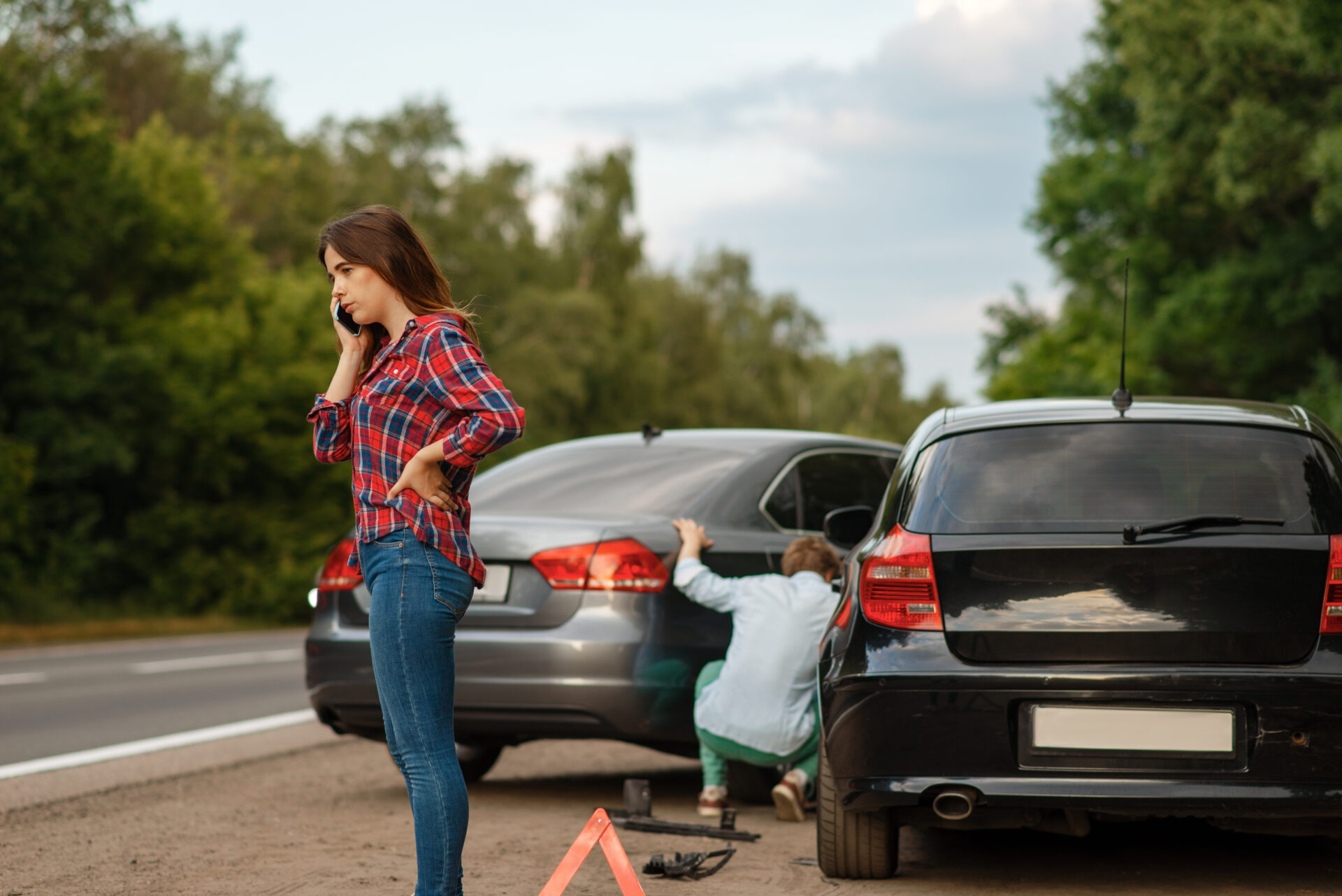 A woman standing next to her car after a car accident, seeking insurance assistance.