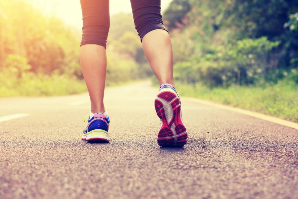 The legs of a woman walking on a road.